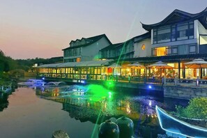 A traditional building with a reflective waterway in front, a bridge, and illuminated windows. - 1881 Peninsula Hotel (Wuxi)