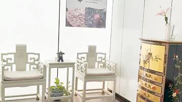 Ein Zimmer mit zwei weißen Stühlen, einem kleinen Tisch und einer Kommode mit floralen Mustern.