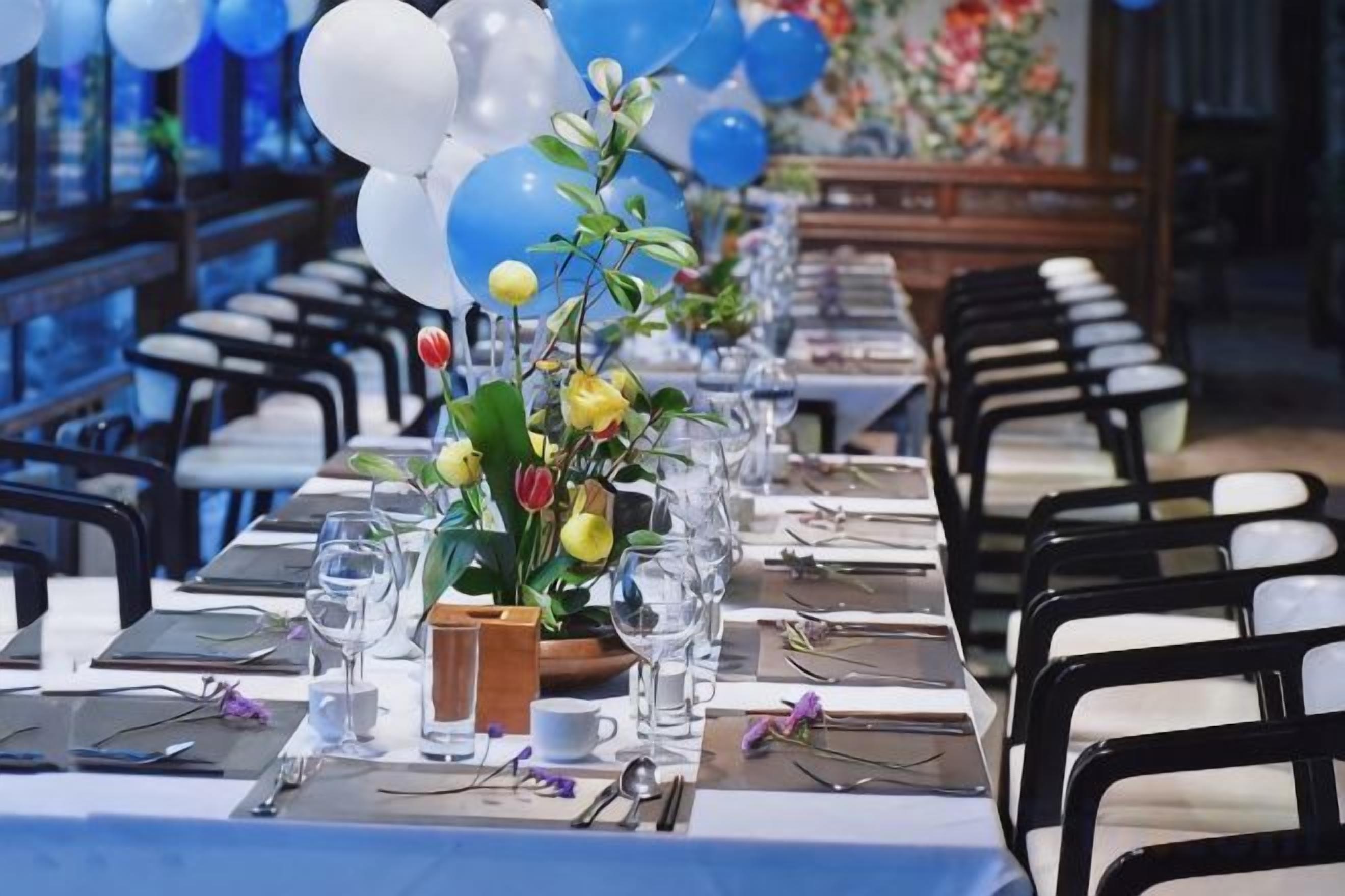 Een feesttafel ingericht met stoelen, een bloevas en een lange tafelkleed.