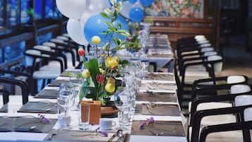 Een feesttafel ingericht met stoelen, een bloevas en een lange tafelkleed.