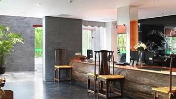 A reception area with a curved counter, several wooden chairs, and a large potted plant.