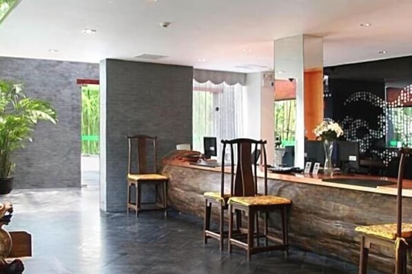 A reception area with a curved counter, several wooden chairs, and a large potted plant. - 1881 Peninsula Hotel (Wuxi)