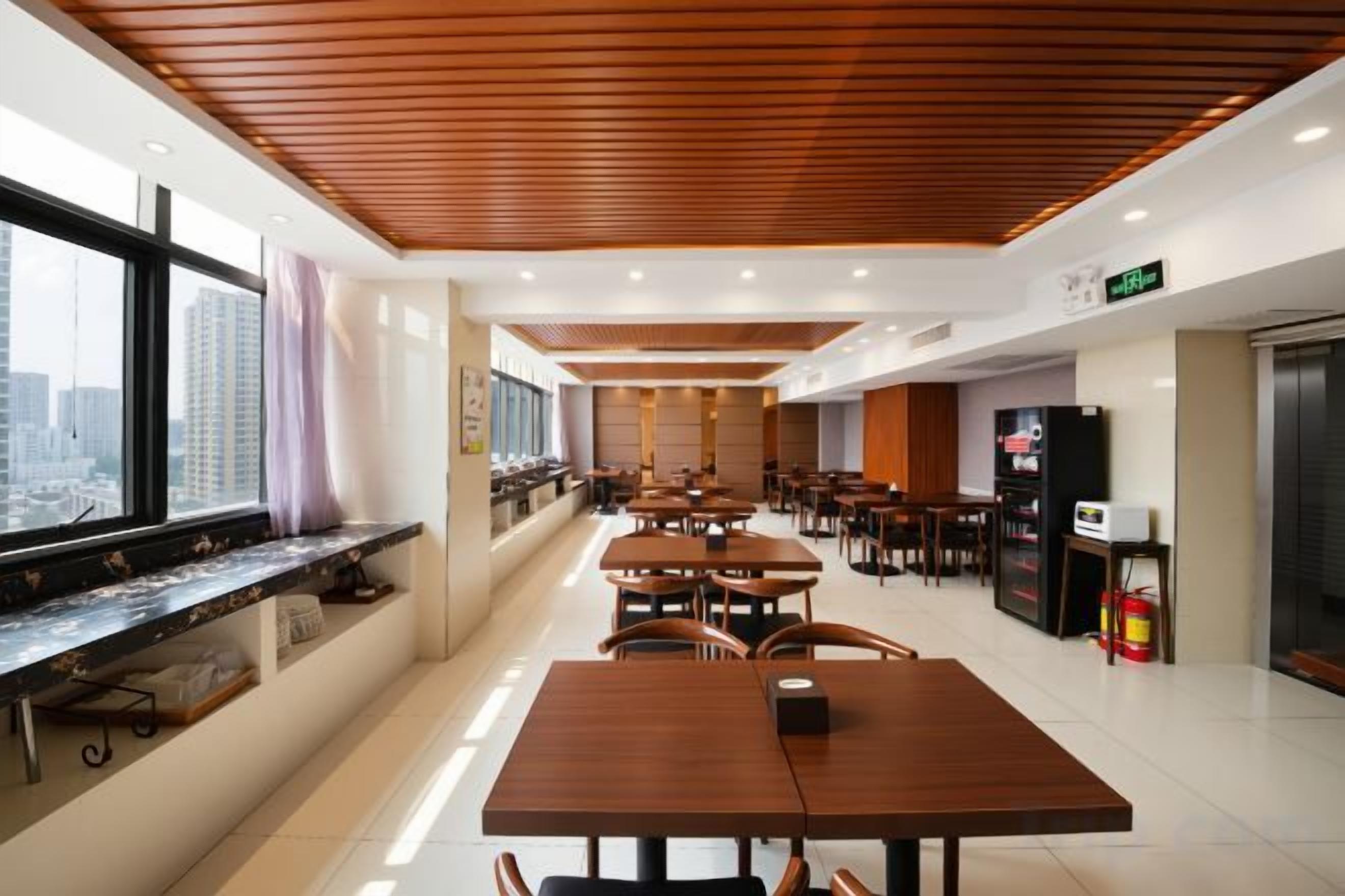 Un comedor moderno con varias mesas y sillas, una barra larga y vistas de la ciudad a través de amplios ventanales.