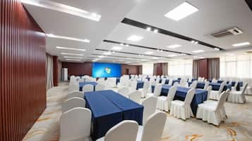 Un salón de conferencias con filas de mesas y sillas, una pantalla grande y suelo alfombrado.