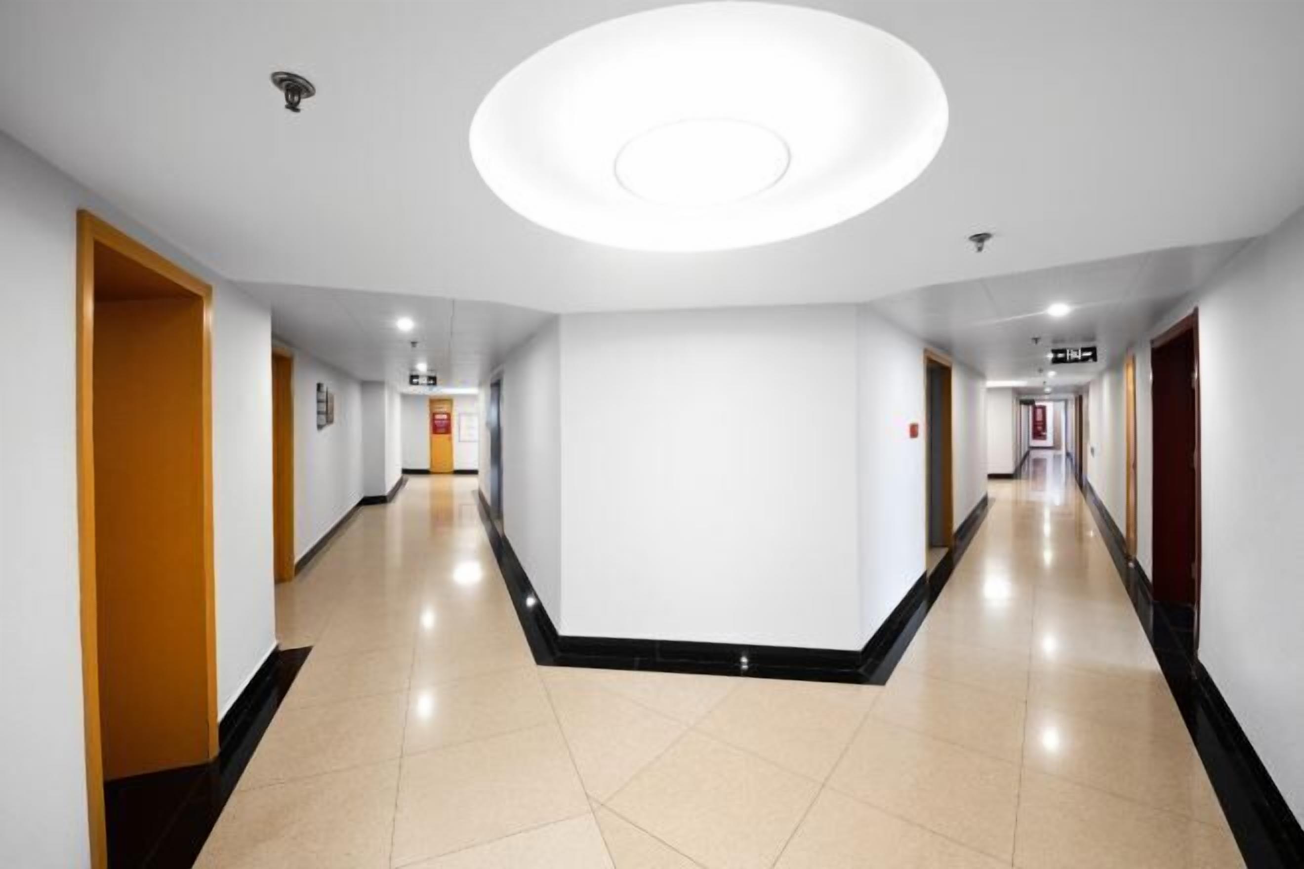 Un pasillo largo y estrecho en un hotel, con puertas a ambos lados, un pasillo central y una lámpara en el techo.