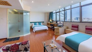 Ein Hotelzimmer mit zwei Betten, einem Schreibtisch, einem Stuhl, einer Glasdusche und Blick auf die Stadt.