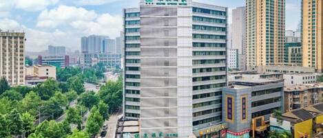 Un edificio de varios pisos con fachada plana, rodeado de otros edificios altos y vegetación.