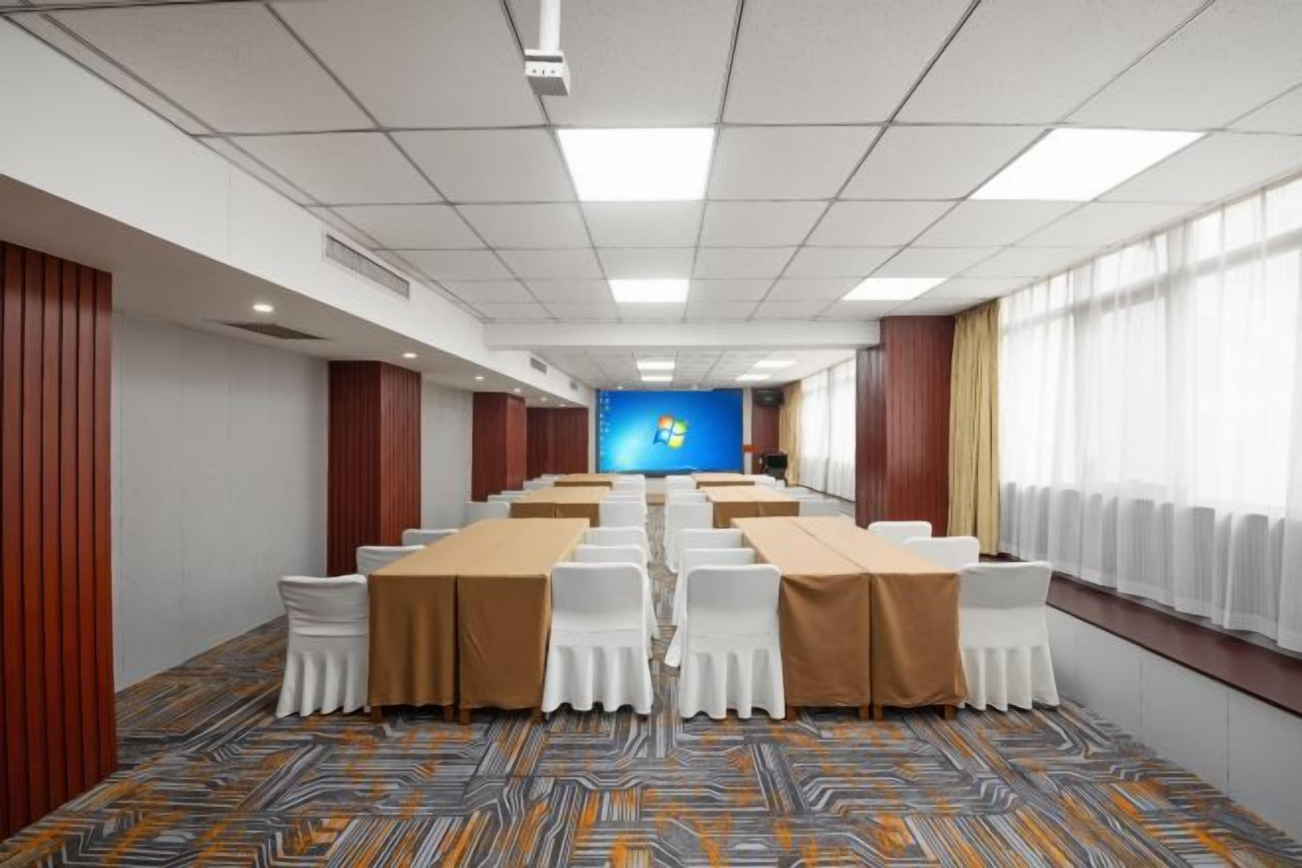 A conference room with a long table, white chairs, and a blue screen at the front.