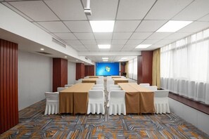 Un salón de conferencias con una mesa larga, sillas blancas y una pantalla azul al frente.