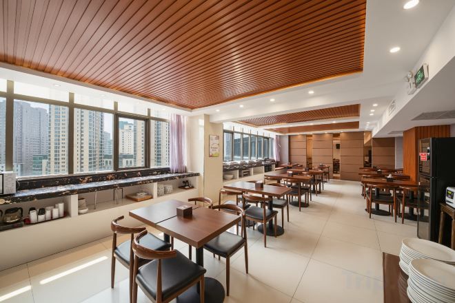 A modern dining area with high tables and chairs, a long counter with a display, and large windows offering a city view.