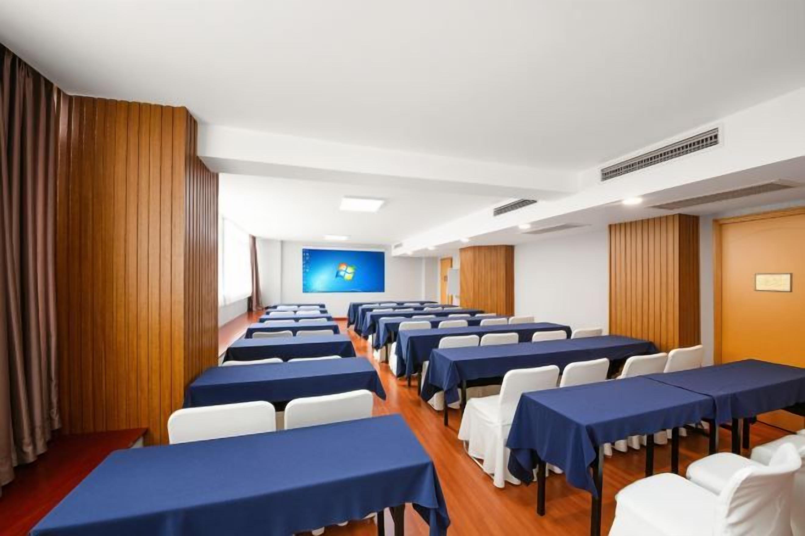A conference room with rows of tables and chairs, a large screen at the front, and wooden paneling on the walls.