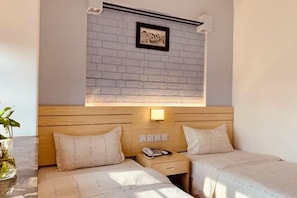 A hotel room with two beds, a wooden headboard, a small table with a vase, and a wall-mounted light fixture.