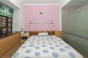 A bedroom with a pink wall, a bed with a patterned bedspread, a bedside table, and a window with a view of greenery. - Fengju Business Hotel (Hourui Metro Station, Shenzhen Airport) (Shenzhen)