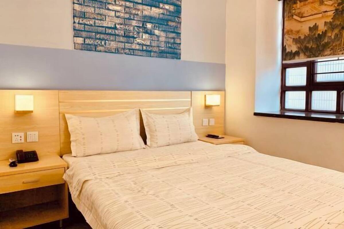 A hotel room with a large bed, two bedside tables, a wall-mounted artwork, and a window with blinds.