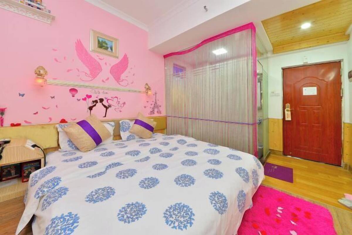 A bedroom with a bed, a wooden door, and a pink wall with decorative elements.