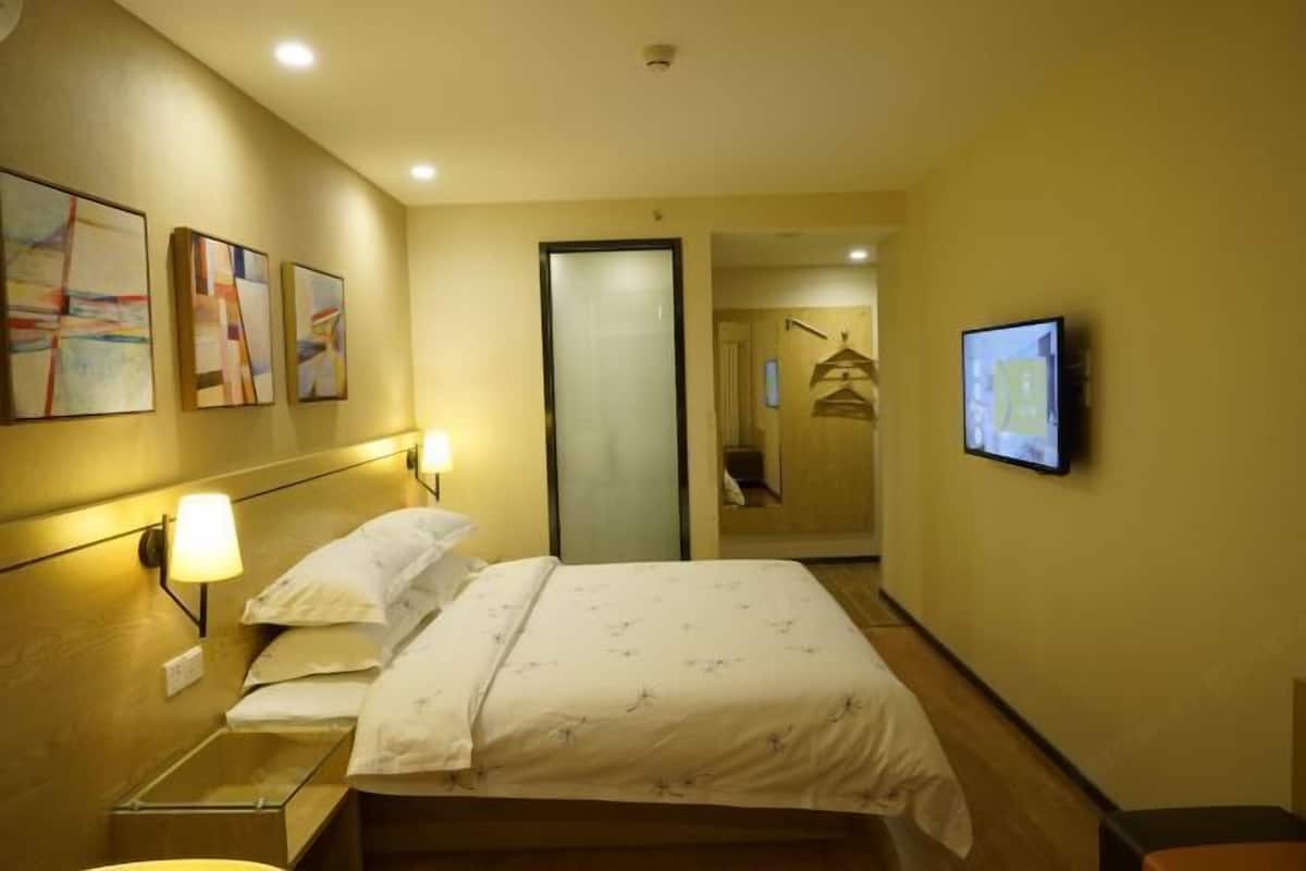 A hotel room with a bed, bedside lamps, a television, and artwork on the walls.