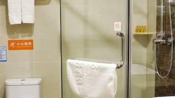 Zona de ducha con mampara de vidrio, una toalla colgada en un perchero, un inodoro y un estante con artículos de aseo.