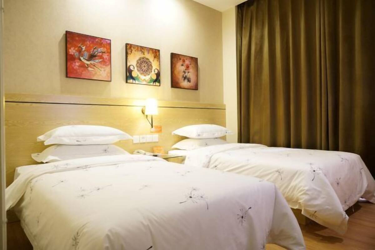 A hotel room with two beds, a nightstand, a lamp, and three wall-mounted paintings.