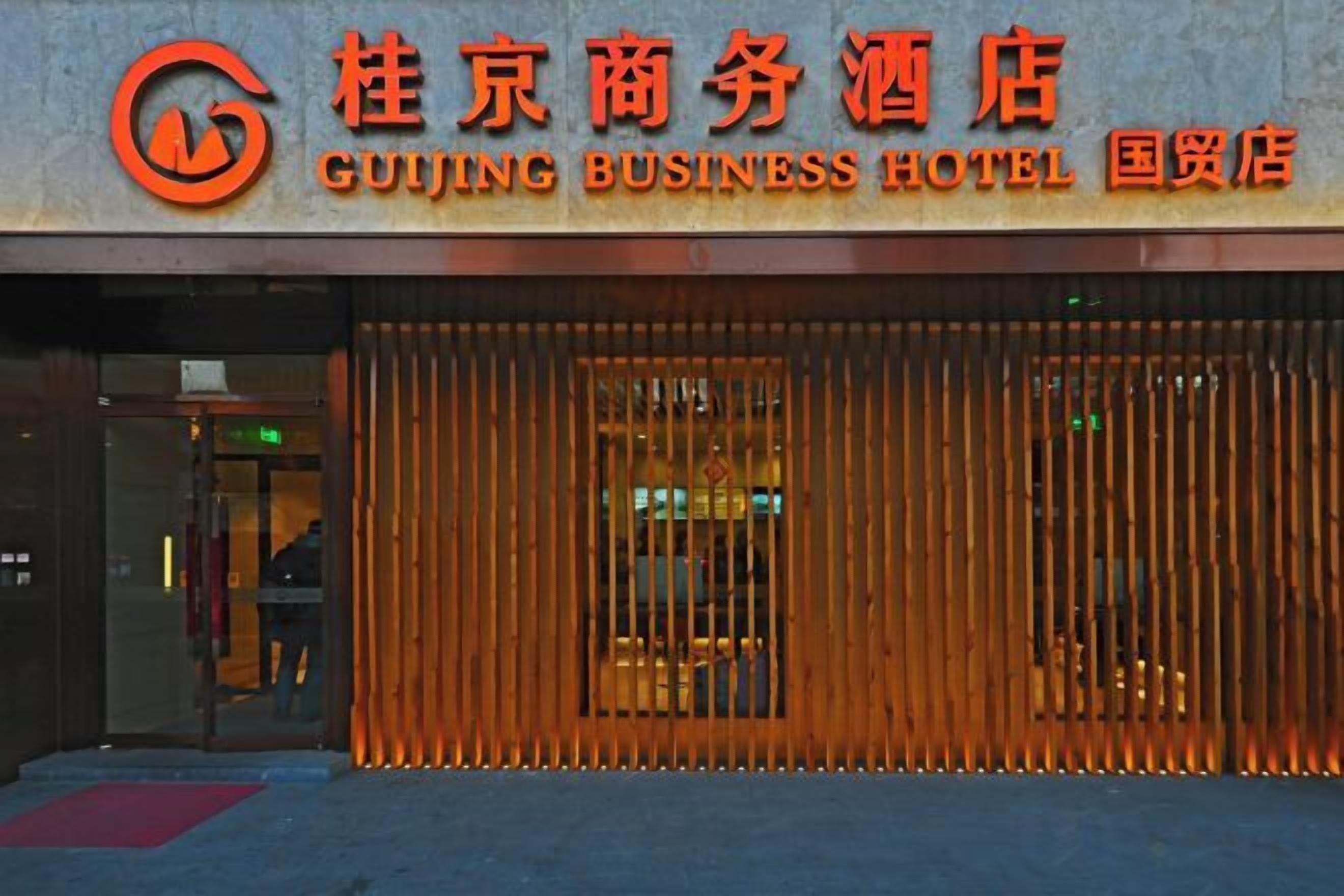 De buitenkant van het Guiqing Business Hotel, uitgevoerd in traditionele Chinese architectuur, met houten lambrisering en een rode loper bij de ingang.