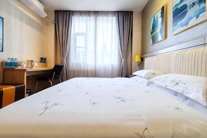 Een hotelkamer met een bed, een bureau, een stoel, een raam met gordijnen en een schilderij aan de muur.
