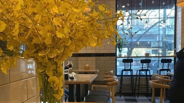 En restaurantindretning med et stort vindue, en vase med gule blomster og en flisebeklædt væg.