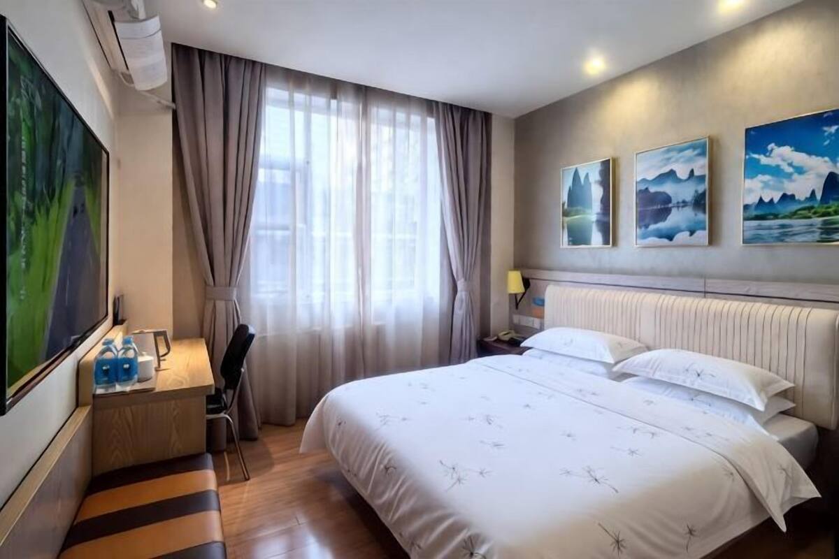 A hotel room with a bed, a desk, a chair, a TV, and a window with curtains.