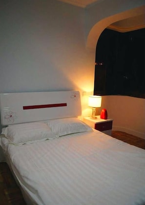 A bedroom with a bed, a nightstand with a lamp, and a window with a dark frame. - Gulangyu Lianhe Apartment Hotel - Xiamen (Xiamen)