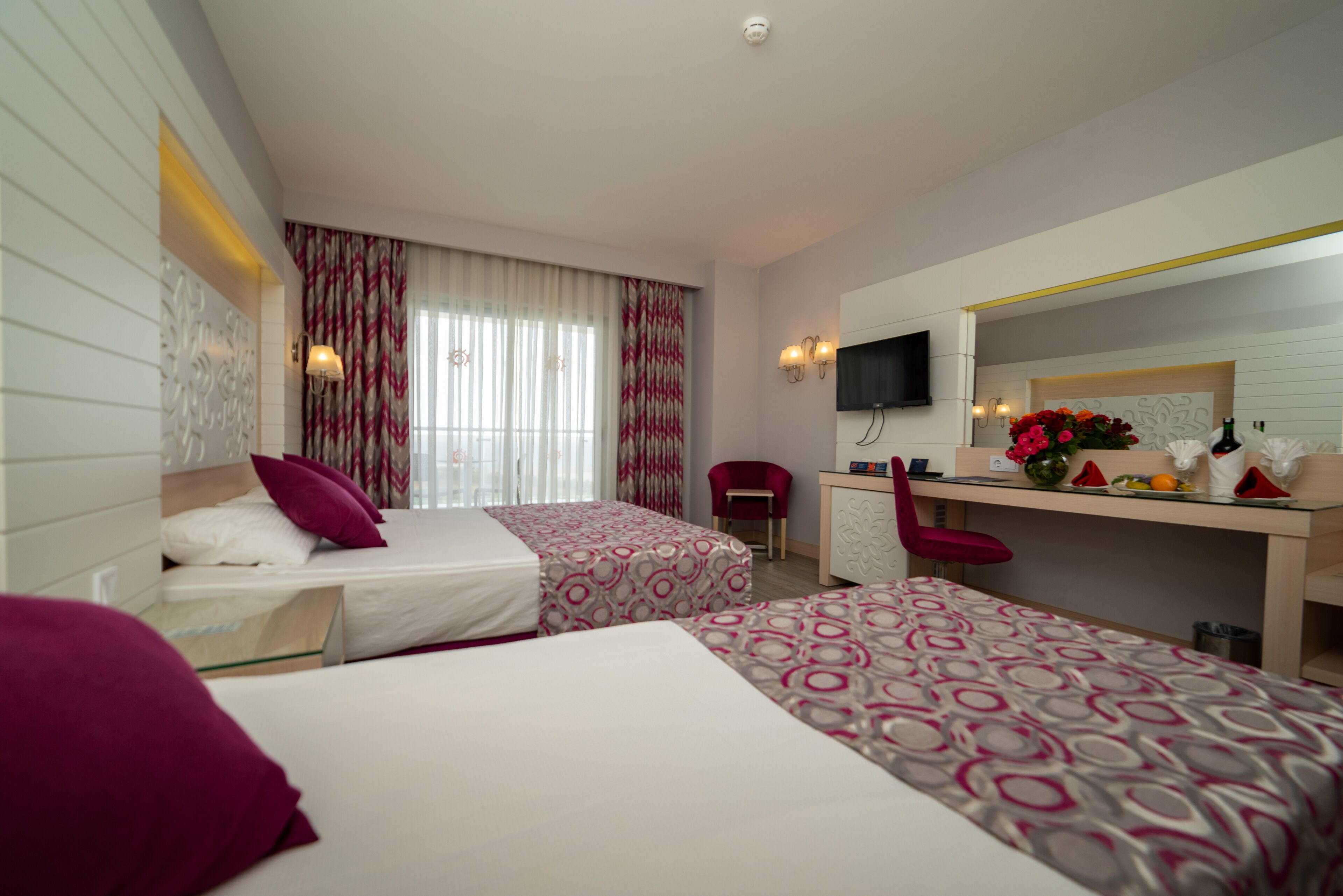 A hotel room with two beds, a desk, a chair, a TV, and a mirror.