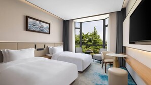 A hotel room with two beds, a small table, a chair, a TV, and a window with a view of trees. - Days lnn by Wyndham Yantai Penglai (Yantai)