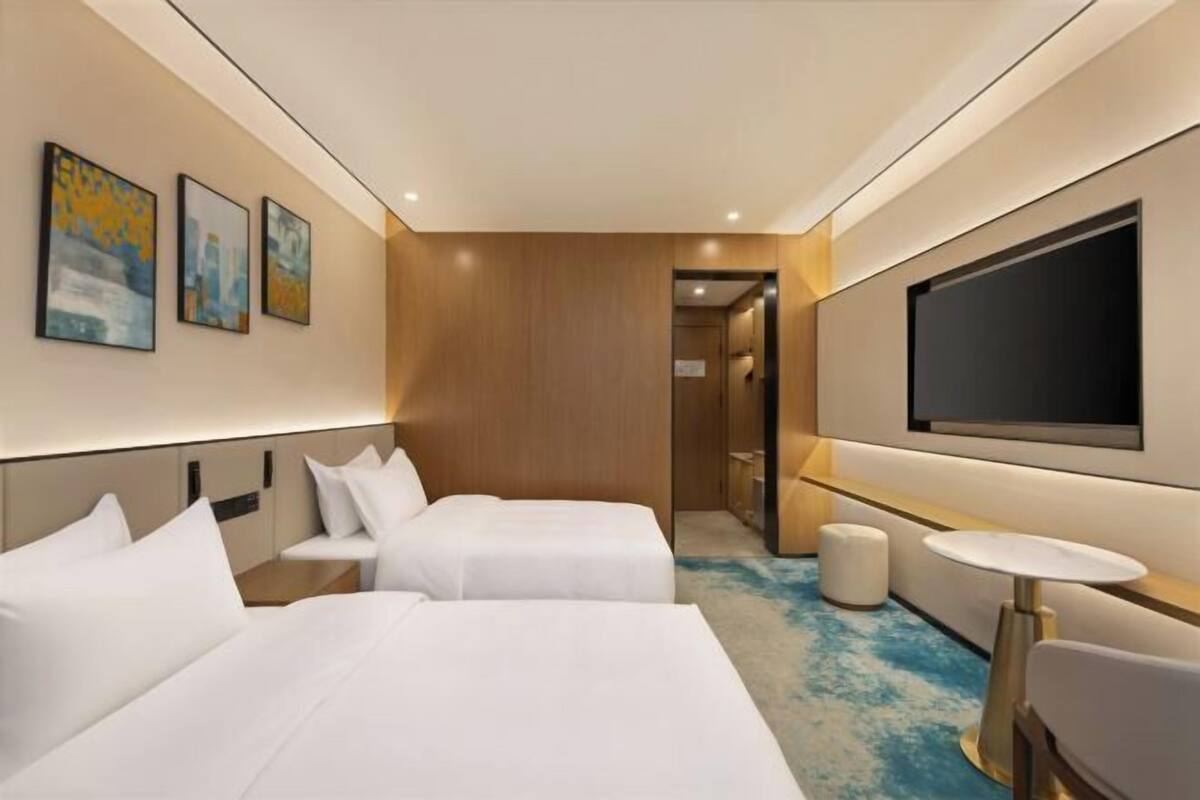 A hotel room with two beds, a small table, a TV, and artwork on the wall.