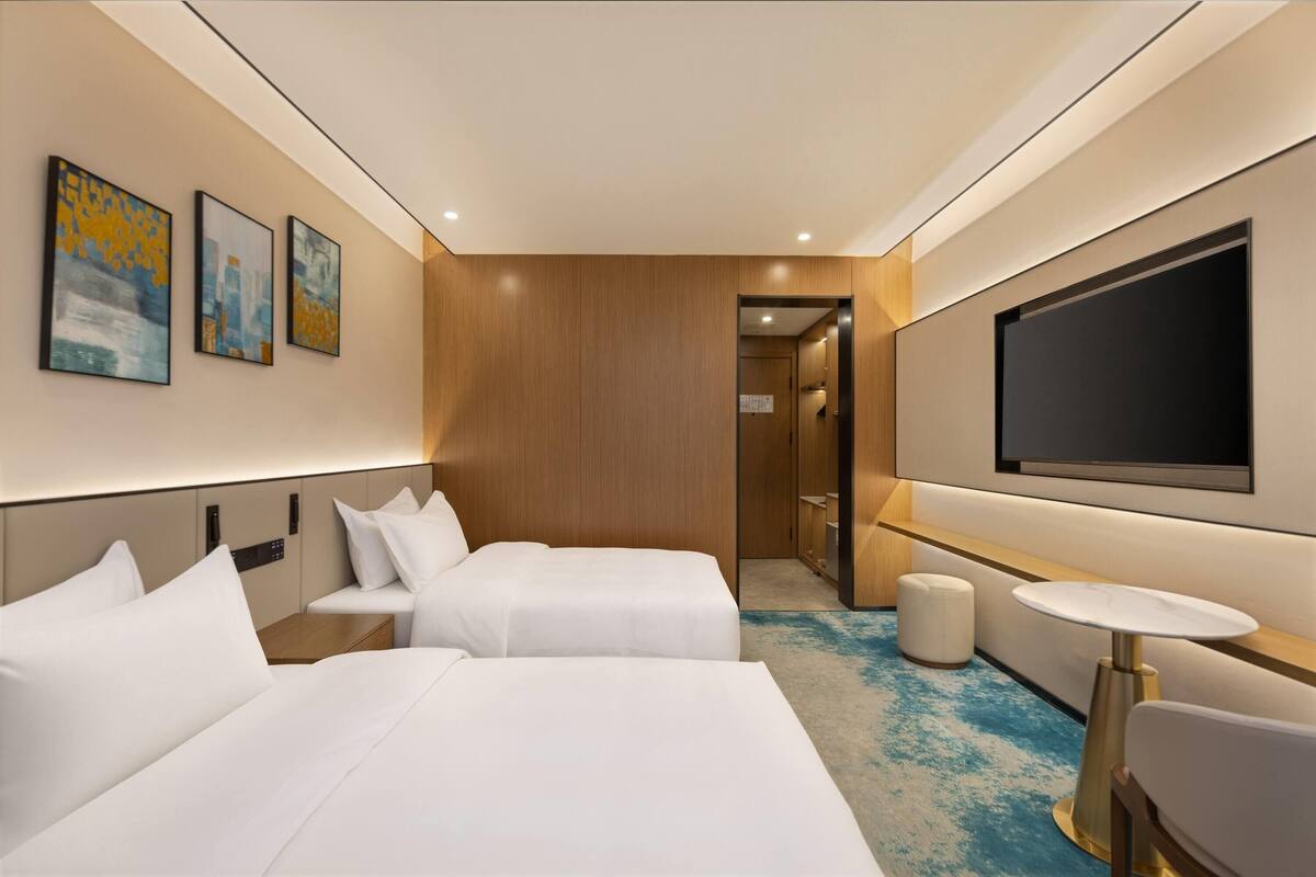 A hotel room with two beds, a TV, a small table, and artwork on the wall.