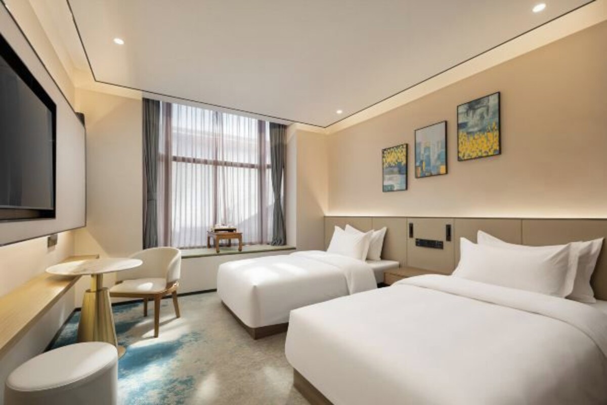 Habitación de hotel con dos camas, televisión, escritorio, silla y ventana con cortinas.