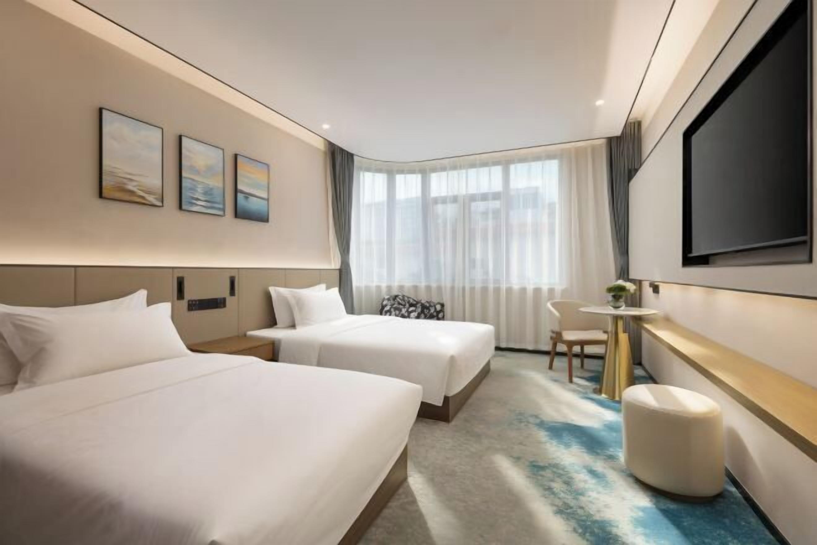 Habitación de hotel con dos camas, televisión, una mesita y ventana con cortinas.