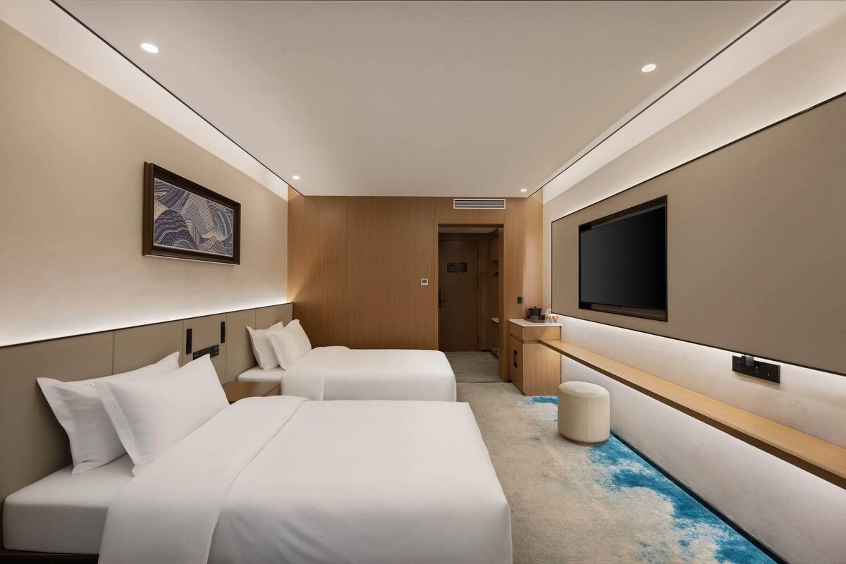 A hotel room with two beds, a TV, a wooden panel wall, and a door leading to the bathroom.
