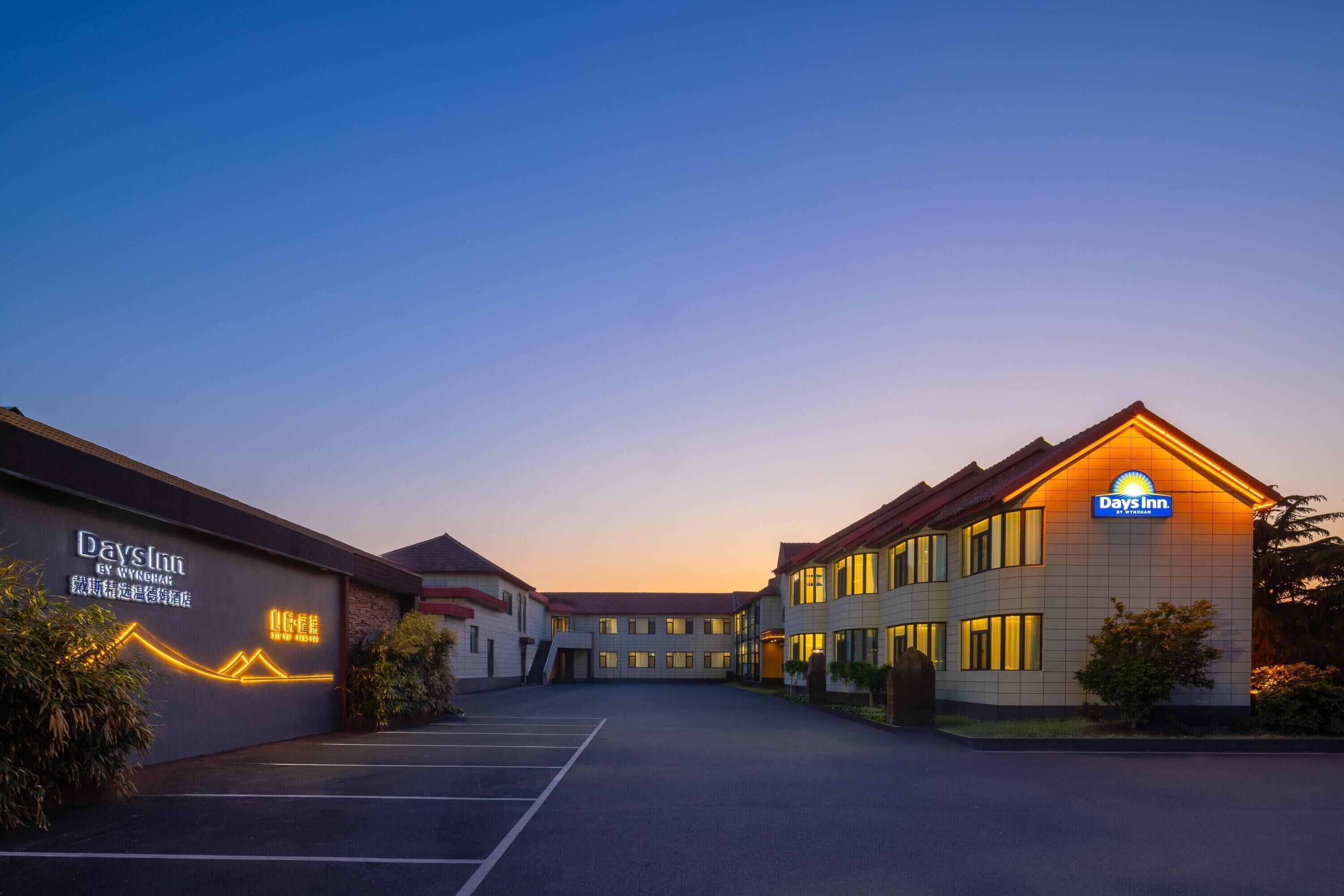 A Days Inn hotel with a parking lot, a building with a sign, and a clear sky.