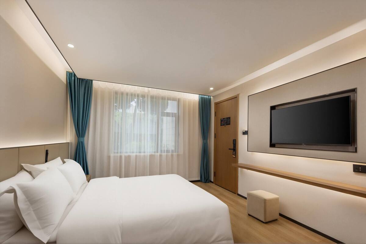 A hotel room with a bed, a television mounted on the wall, a door, and a small bench.