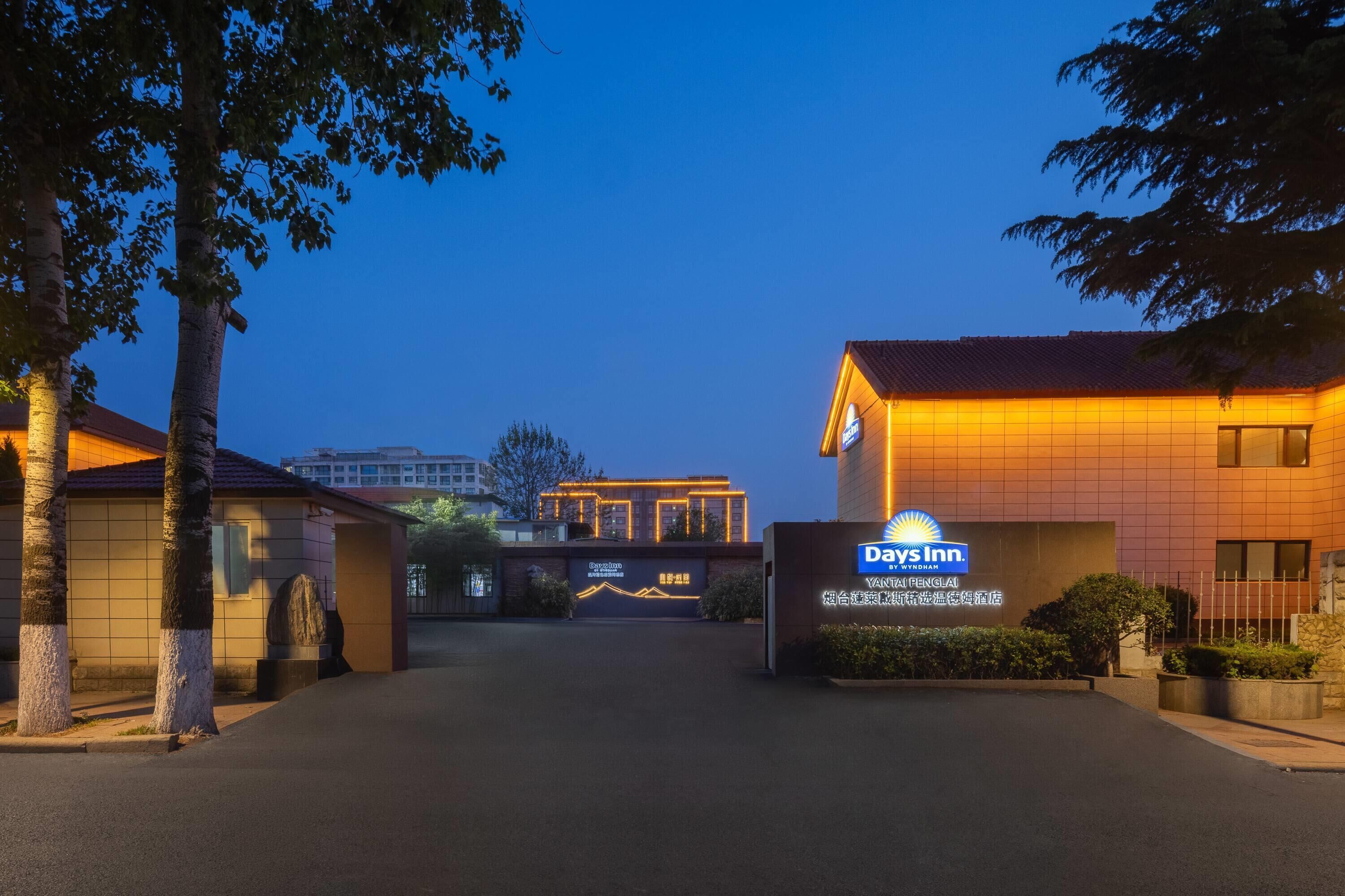 Entrada de hotel con el letrero de Days Inn, fachada con azulejos y cielo despejado.