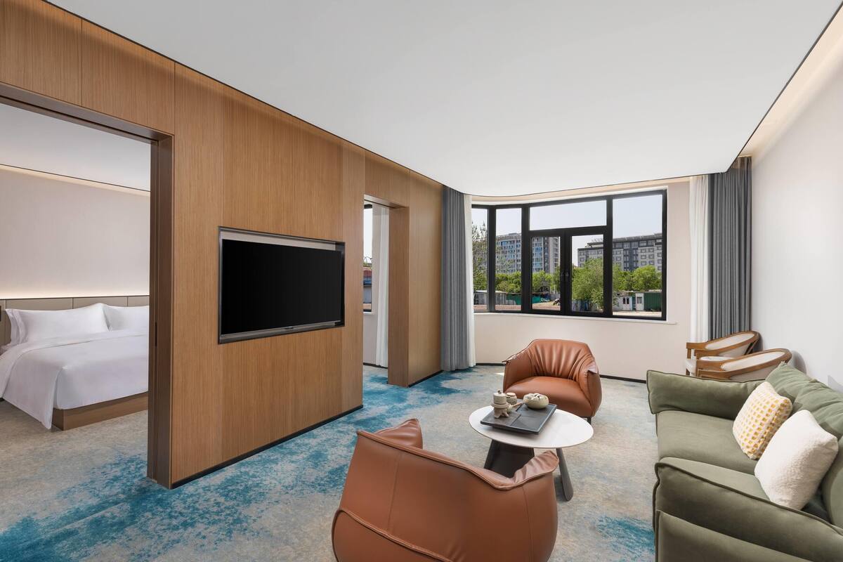 A hotel room with a bed, a TV, a seating area with a table, and large windows.