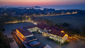 A hotel with multiple buildings, a parking area, and a view of the sea at dusk. - Days lnn by Wyndham Yantai Penglai (Yantai)