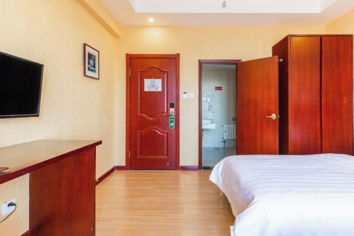 A hotel room with a wooden bed, a TV mounted on the wall, and a wooden wardrobe.