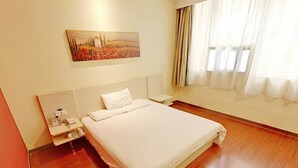 A hotel room with a large bed, a bedside table with a phone and a lamp, a painting on the wall, and a window with curtains. - Hanting Hotel (Zibo)