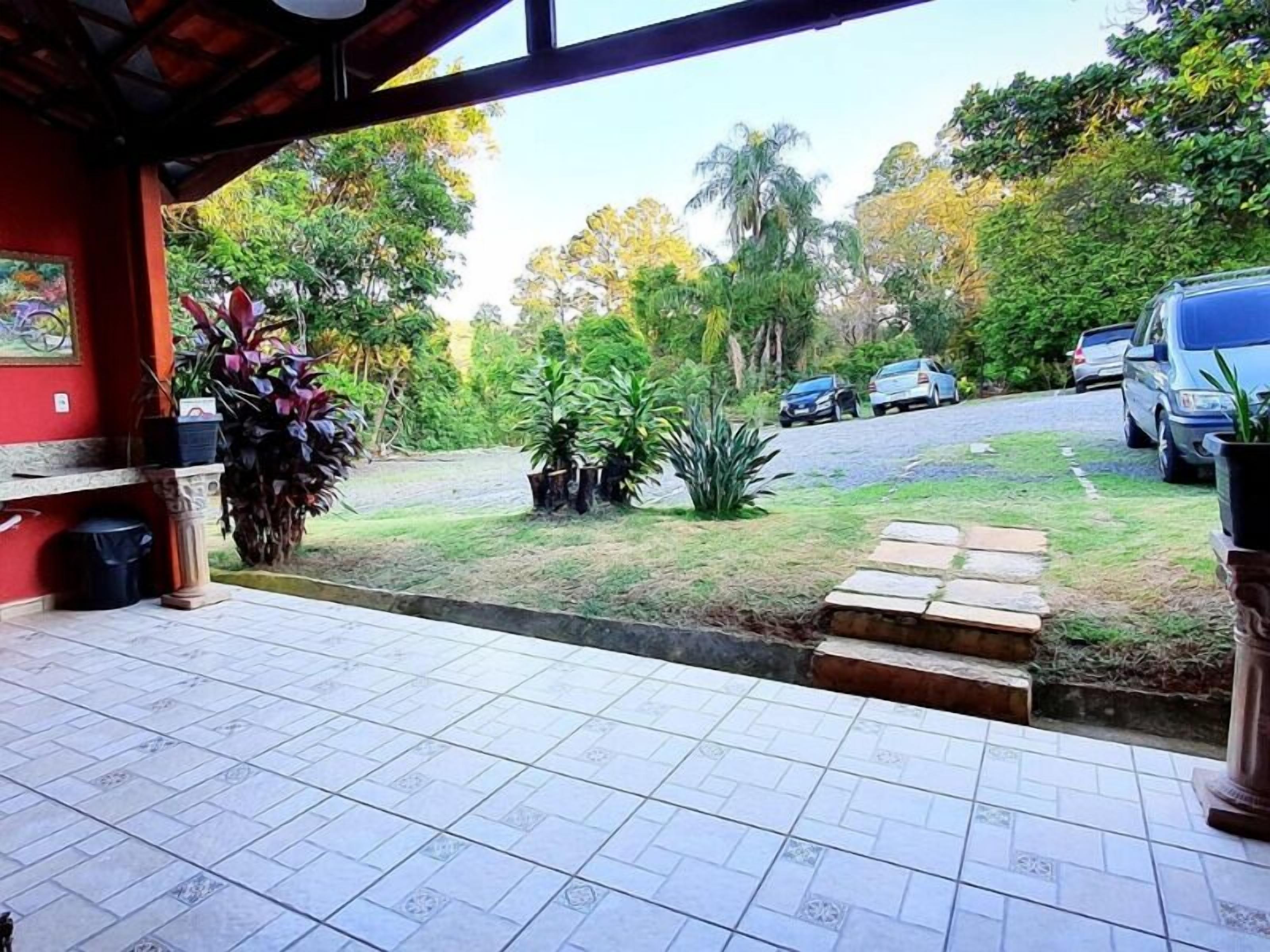 A covered outdoor area with tiled flooring, a bench, potted plants, and a view of a road with parked cars.