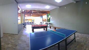 A room with a ping pong table, a pool table, and a dining area with chairs and tables.