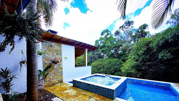 A pool area with a stone and wooden deck, a hot tub, and lush greenery. - Pousada Della Vegas (Serra Negra)