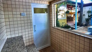 A bathroom with a tiled floor, a granite countertop, a metal door, and a window with a view of an outdoor area. - Pousada Della Vegas (Serra Negra)