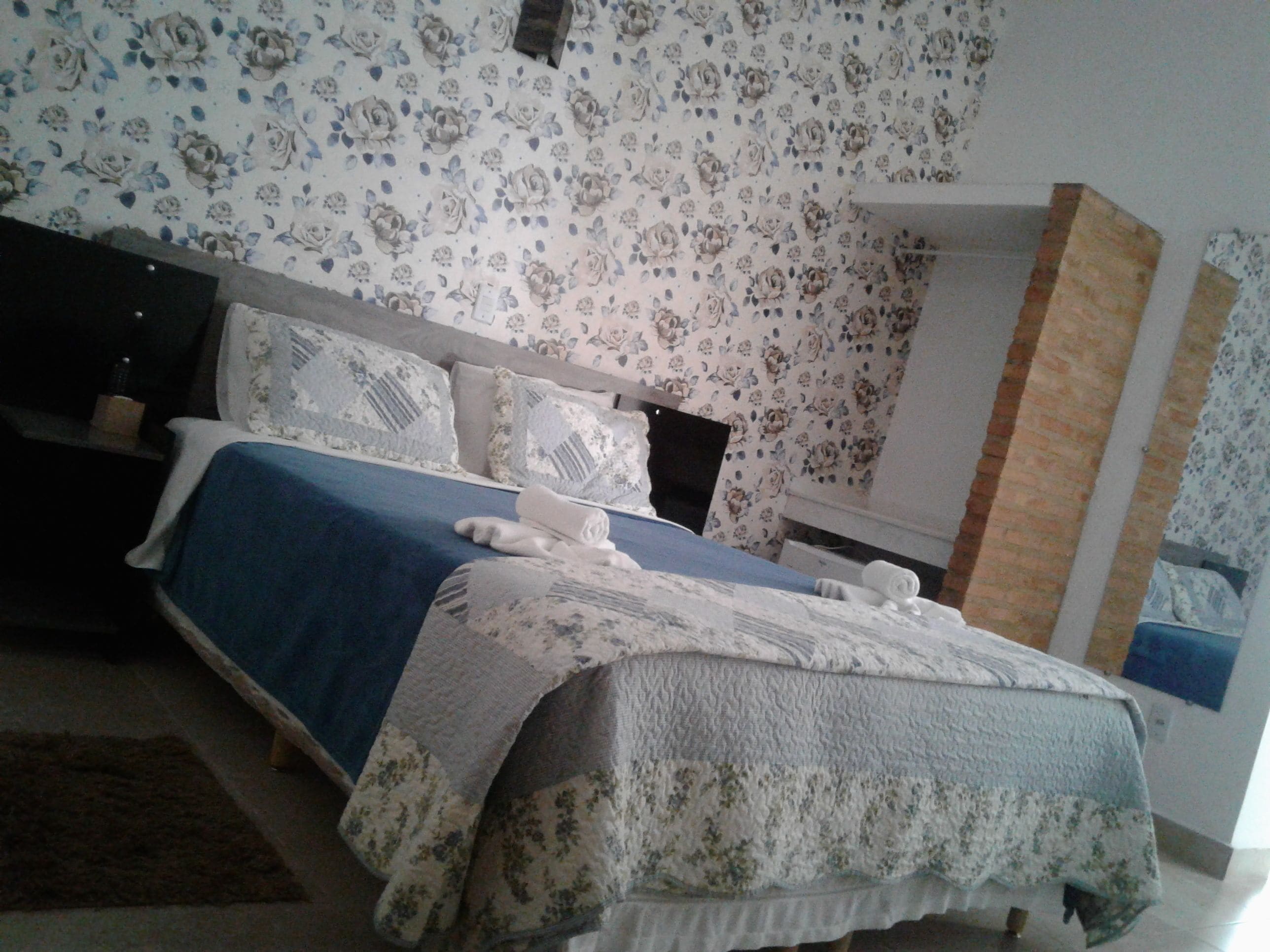 A bedroom with a bed, pillows, a nightstand, and a wall with floral wallpaper.