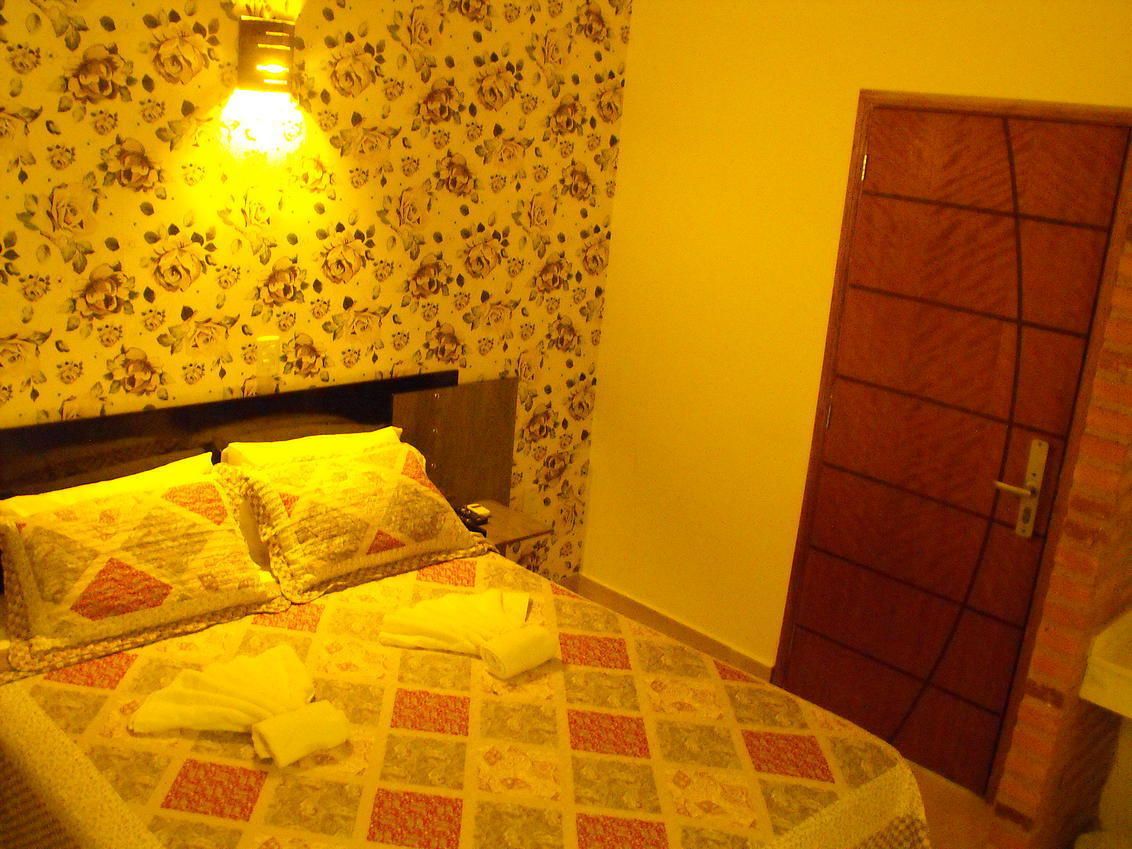 A bed with a floral-patterned bedspread, a bedside lamp, and a door with a red and brown pattern.