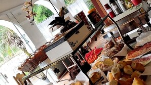 A buffet with various food items, including bread and pastries, under a covered area with wooden beams and a decorative tree mural. - Pousada Della Vegas (Serra Negra)