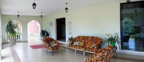 A spacious lobby with a sofa and chairs, potted plants, and a large window.