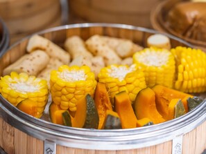 Un plateau de service en bois avec des épis de maïs et divers légumes.